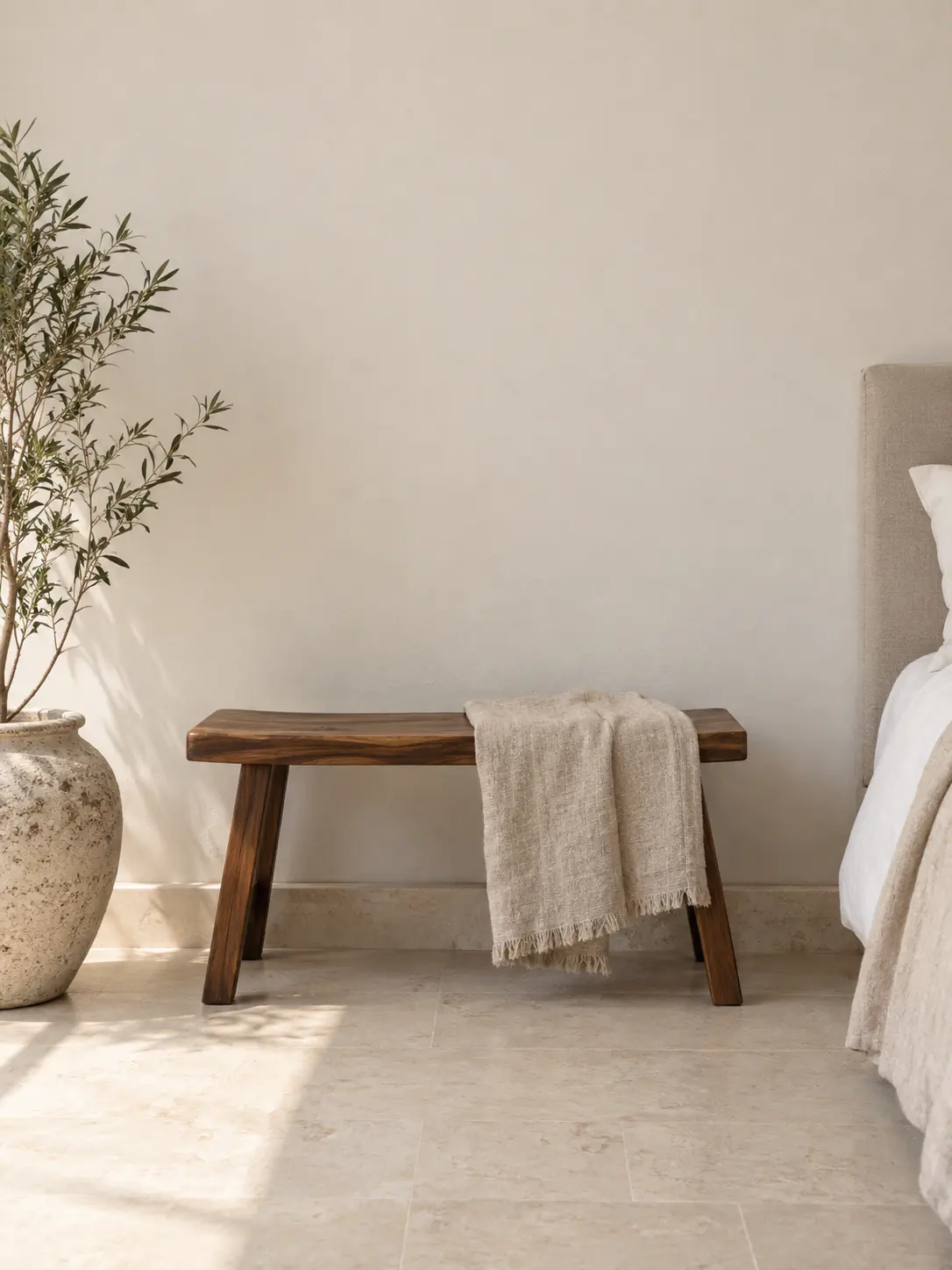 A styled bedroom corner with layered linen and a low walnut stool