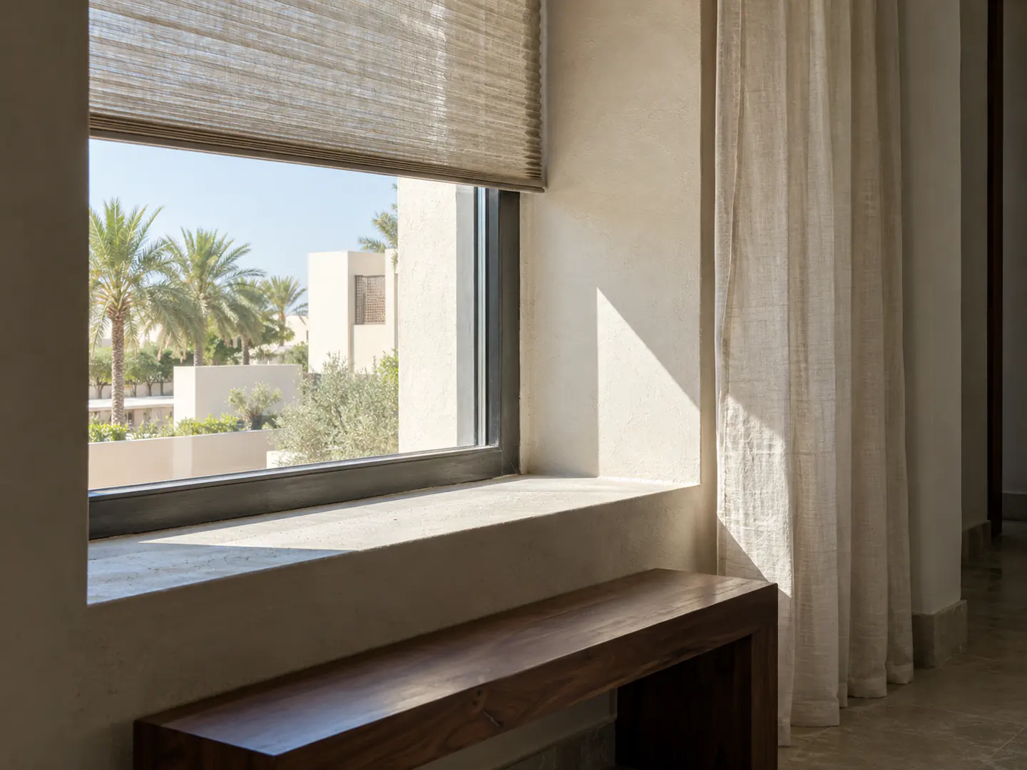 A deeply shaded Dubai window with lightweight linen and a walnut bench